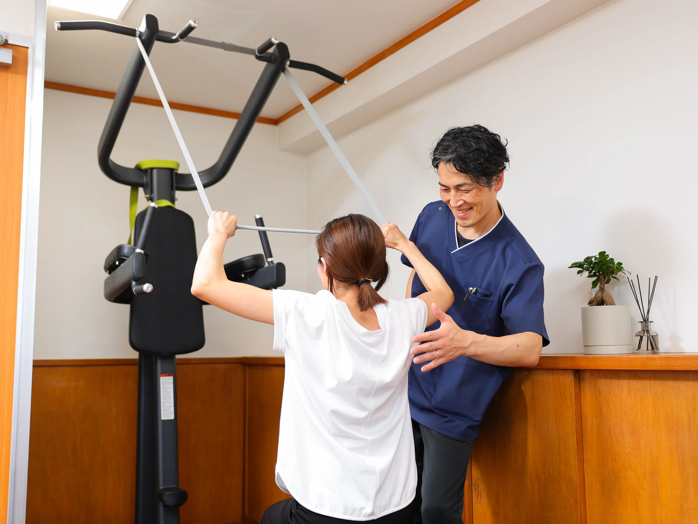 トレーニング機器で運動する女性にトレーナーが姿勢を確認している様子