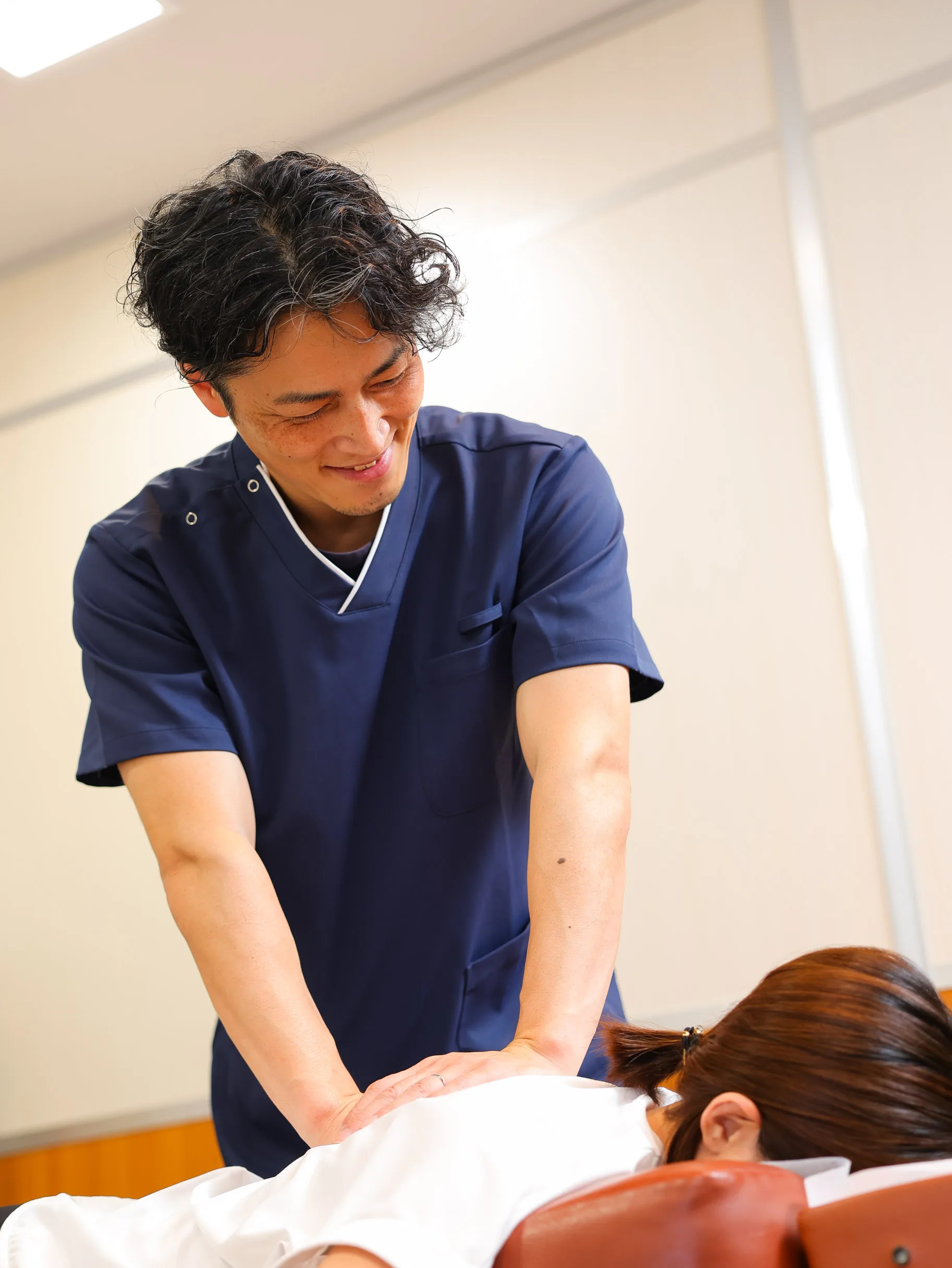 施術ベッドで利用者の背中に手を添えてスタッフが施術している様子
