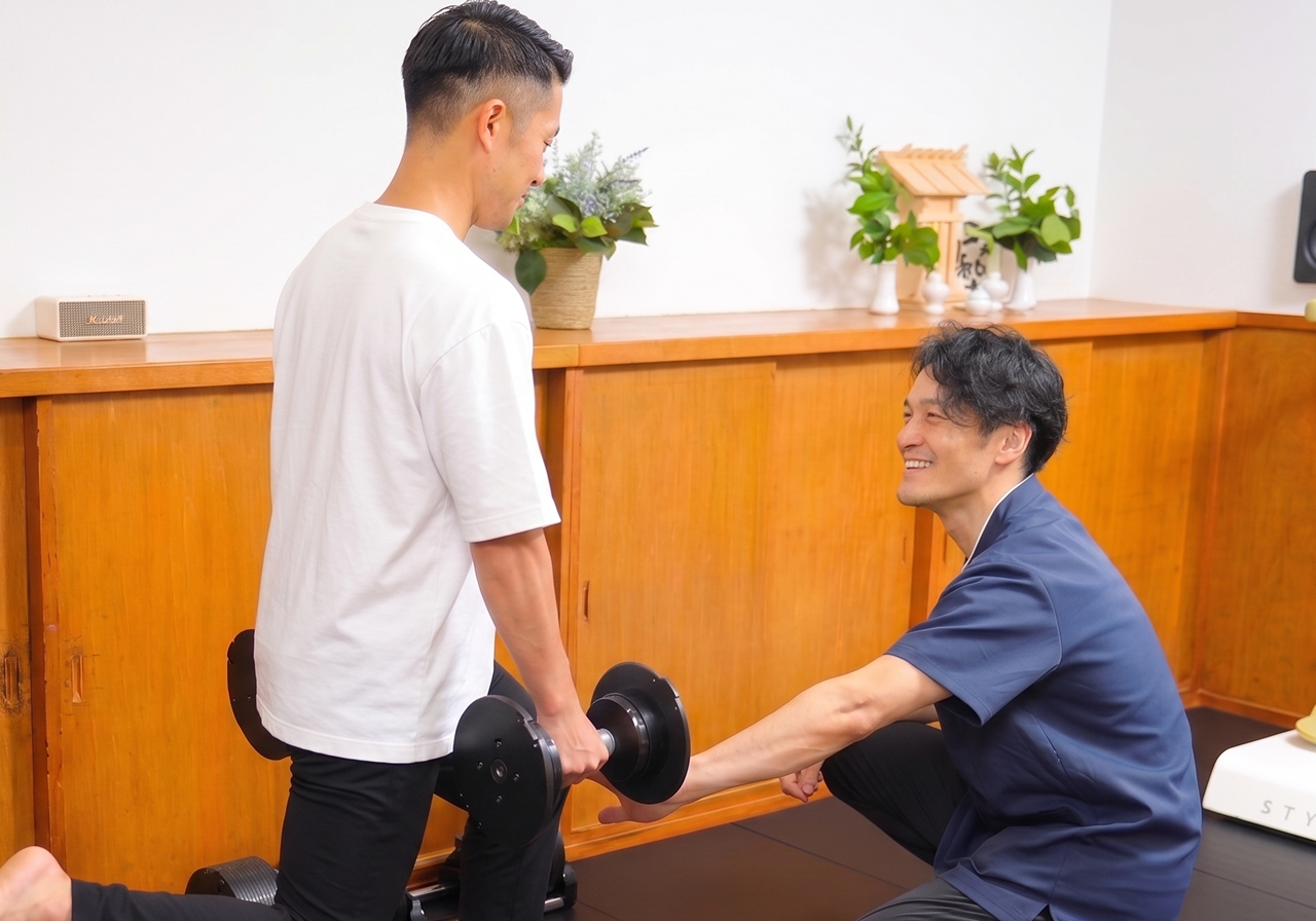 マットの上で利用者が片脚立ちを行い、トレーナーが体幹の安定を確認しているトレーニング風景