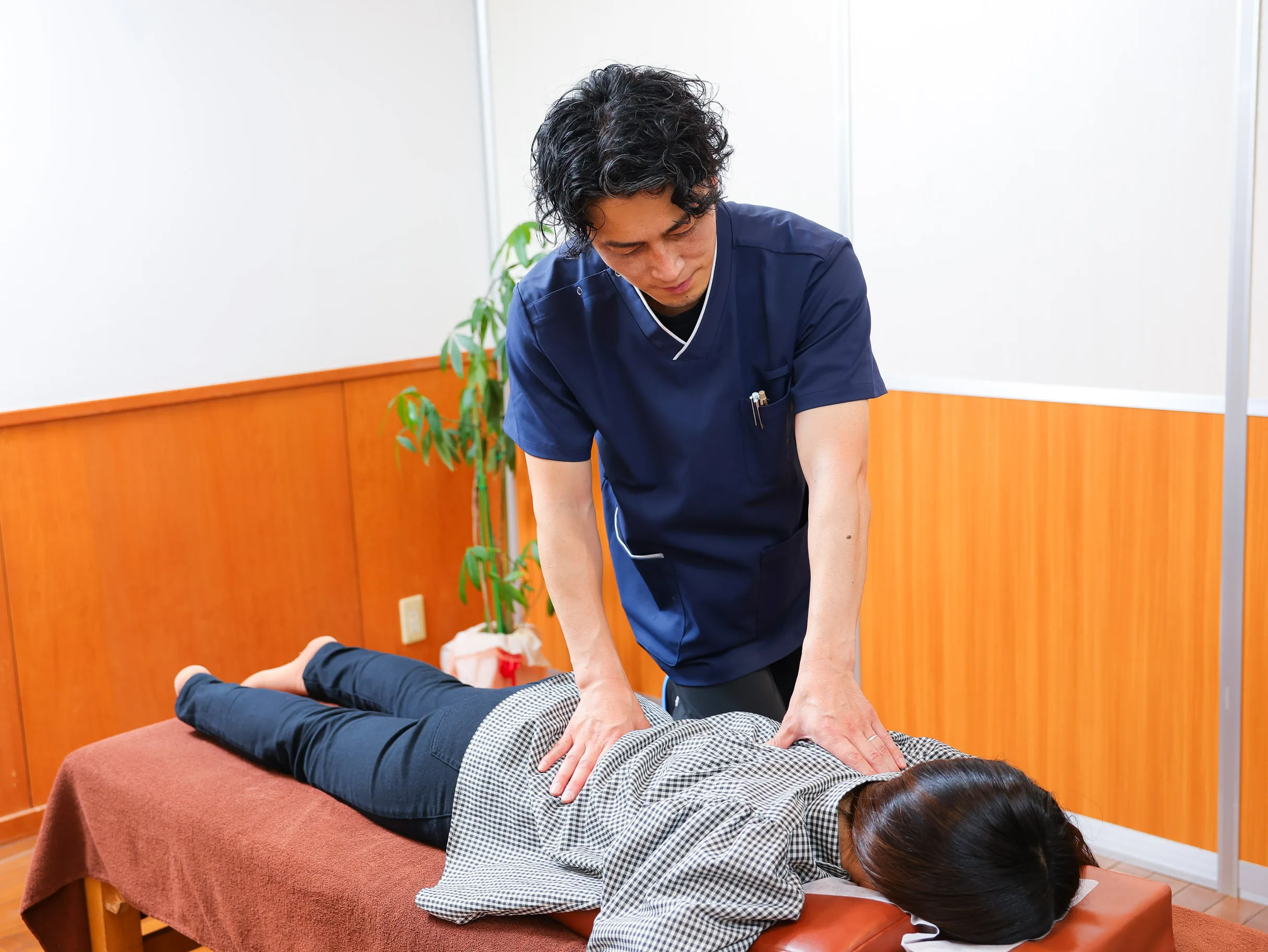 施術ベッドで利用者の背中に手を添えてスタッフが施術している様子