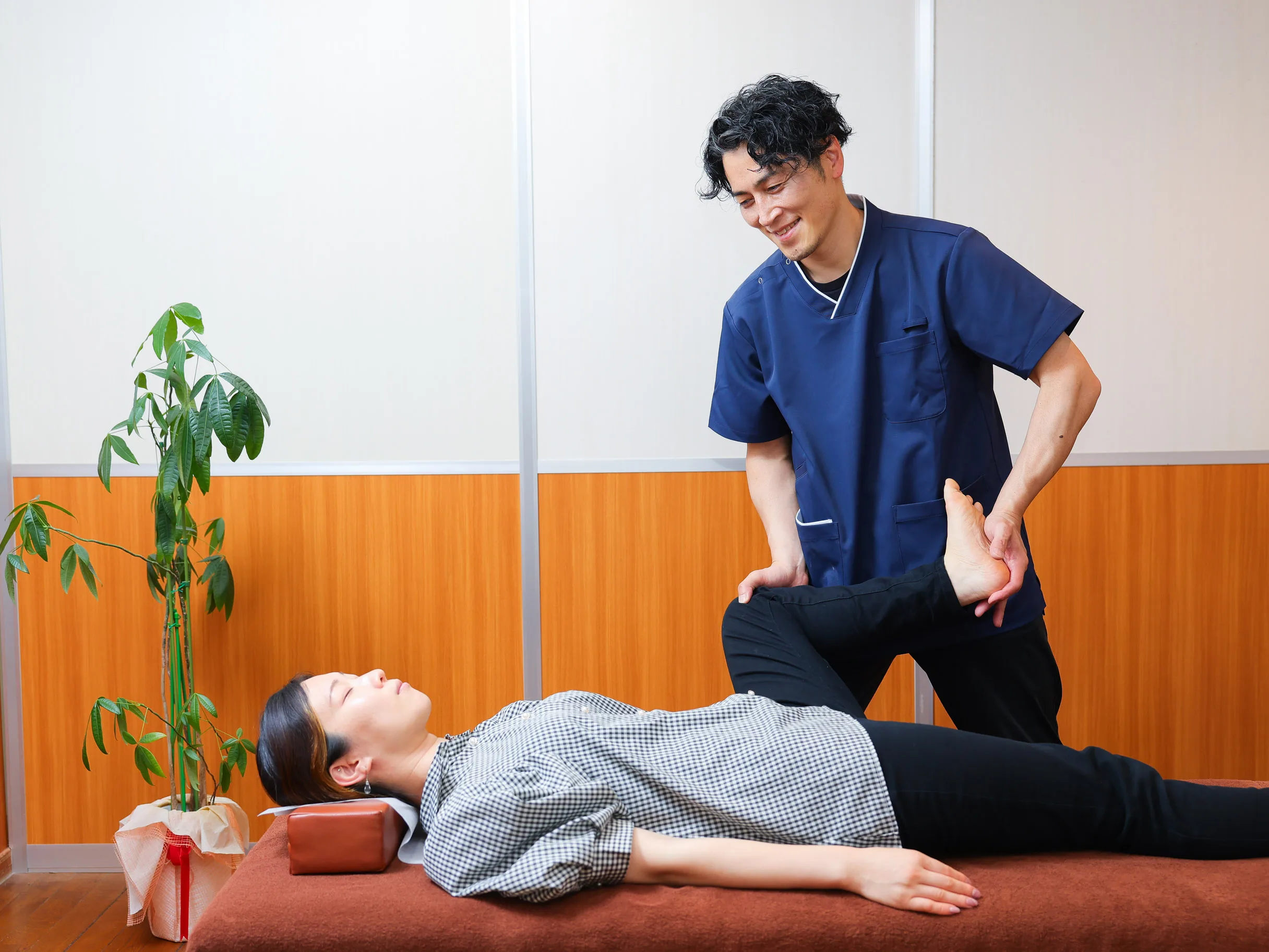 施術ベッドで利用者の脚を確認しながらスタッフが施術している様子