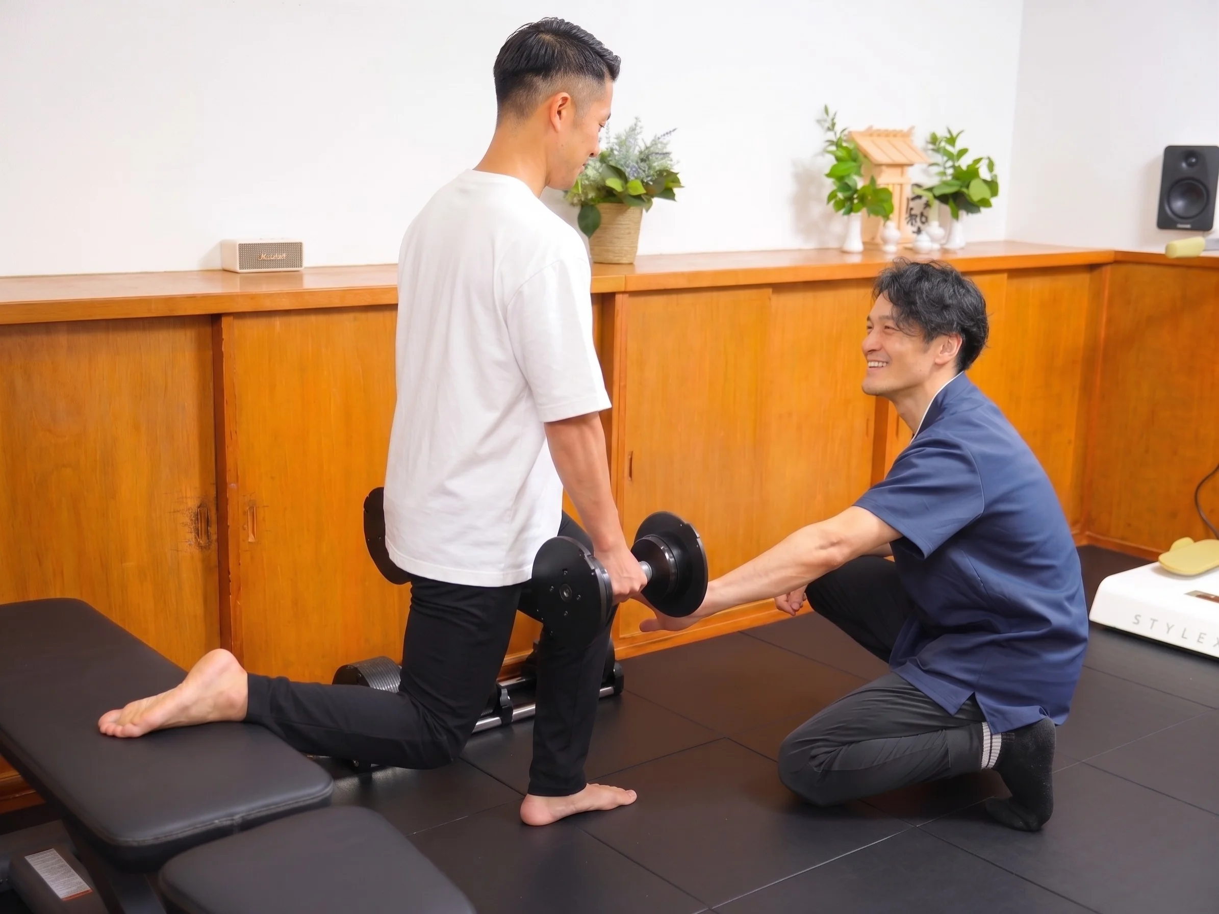 トレーニングベンチの横でトレーナーが利用者の姿勢を確認しながら骨盤の位置を説明している場面
